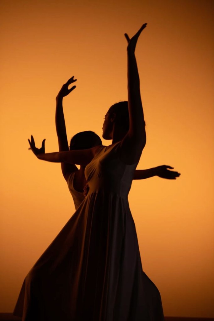 Two dancers in silhouette against a warm orange backdrop